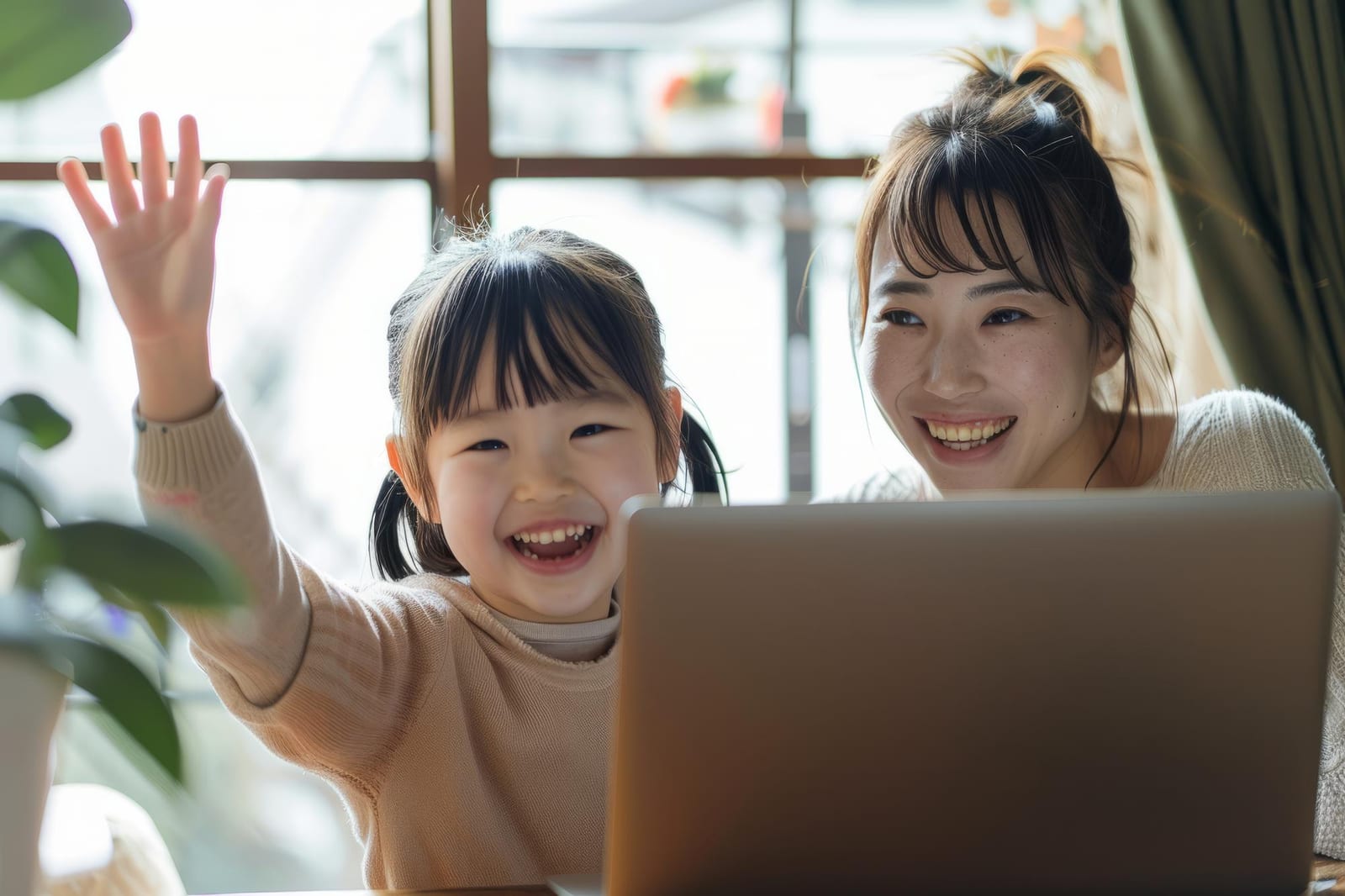 母親と娘がノートパソコンのビデオ通話で手を振る様子