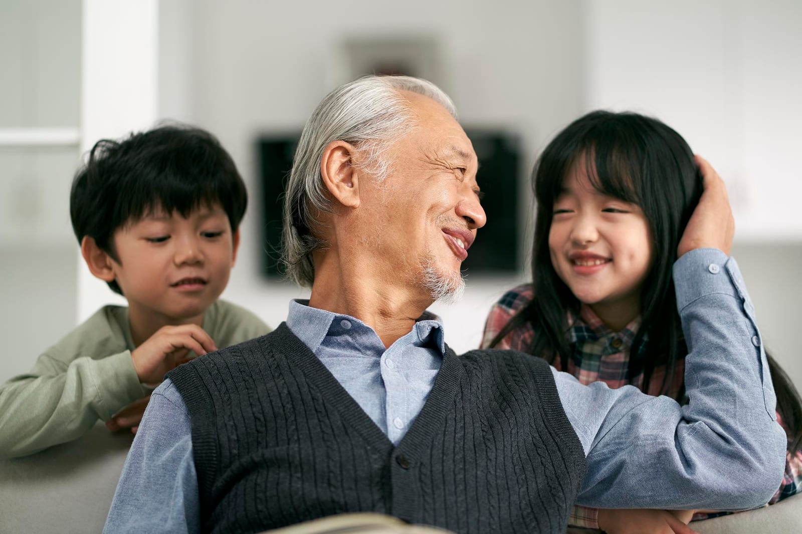 祖父が二人の孫と自宅で座っている様子